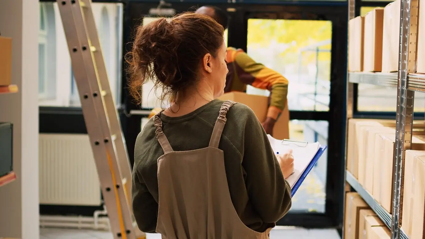 Lagerleiter überprüft die Produktliste im Lagerraum, arbeitet an Logistik und Bestandsinventur mit Kartons auf Regalen. Weibliche Mitarbeiterin analysiert Frachtware zur Qualitätskontrolle.